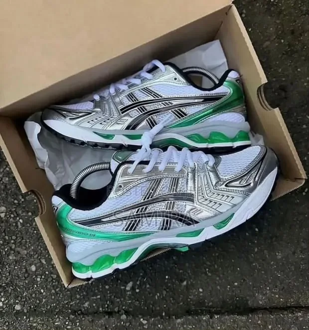 ASICS GEL-KAYANO 14 White / Slate Grey — Chaussures Oriol Shoes Abomey-Calavi. Paire de baskets basses de style running, empeignes en mesh blanc, empiècements argentés et gris, motifs linéaires noirs, détails vert vif sur la tige et la semelle, lacets blancs, semelles épaisses crantées, présentées dans une boîte en carton avec embauchoirs métalliques visibles