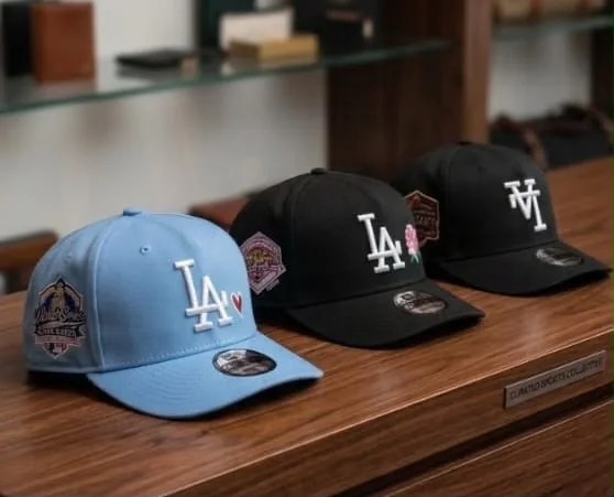 Casquettes & chapeaux chez Oriol Shoes Abomey-Calavi — Trois casquettes de baseball à visière courbée, une bleu ciel avec logo blanc LA et deux noires avec logos blancs LA et NY, avec écussons latéraux et stickers visibles sur les visières